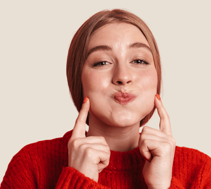 smiling woman pointing at her cheeks for buccal fat pad reduction surgery