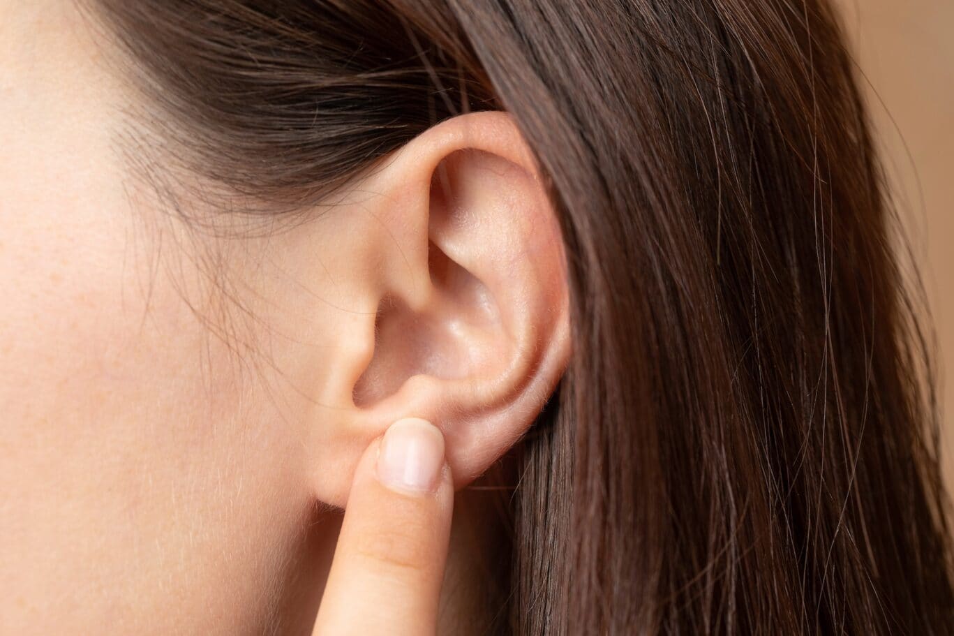 A close-up of a person’s ear with long brown hair, as a specialist gently touches the earlobe, highlighting the precision often associated with plastic surgery.