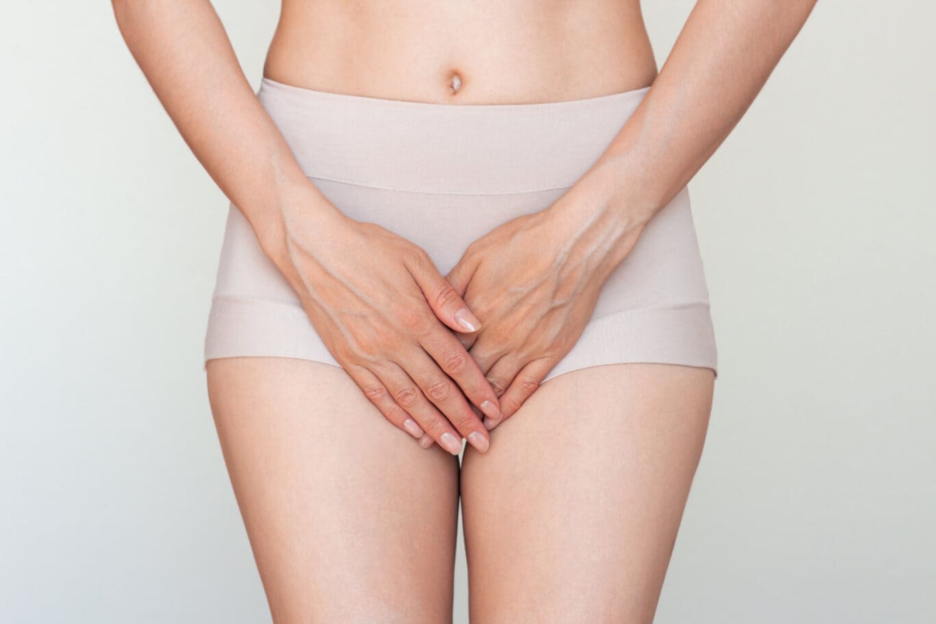 Young Caucasian woman in beige underwear holding her crotch with her hands.