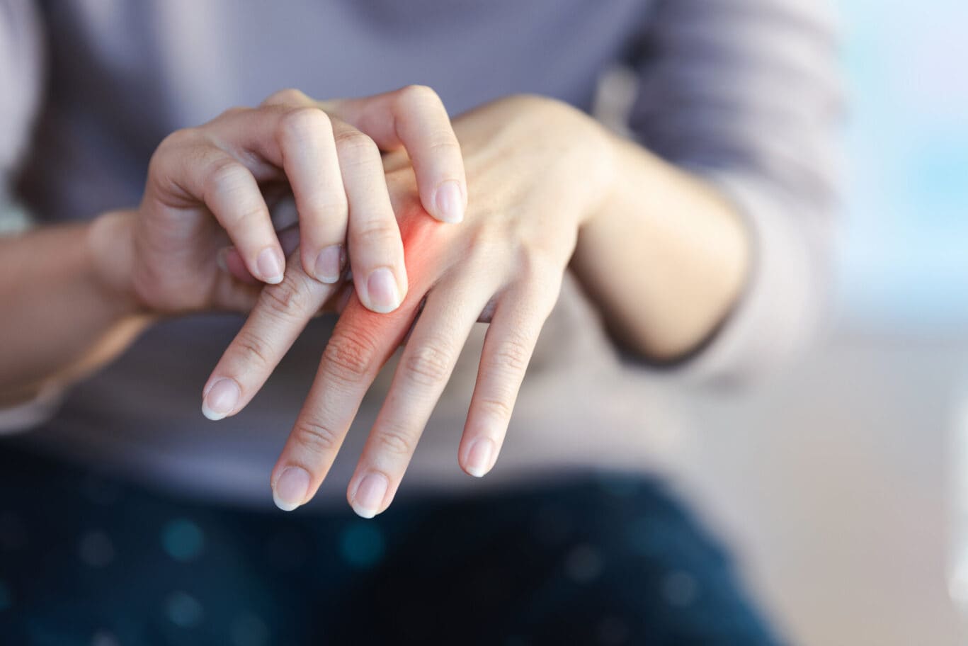 A person touches the back of their hand, highlighting a red, irritated area, possibly indicating pain or inflammation that may require attention from a specialist.