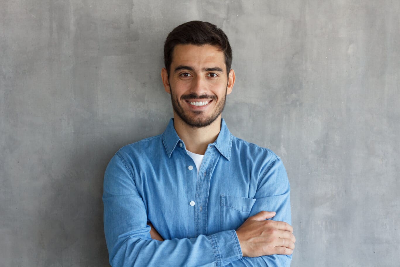 Smiling man in blue shirt, standing with crossed arms