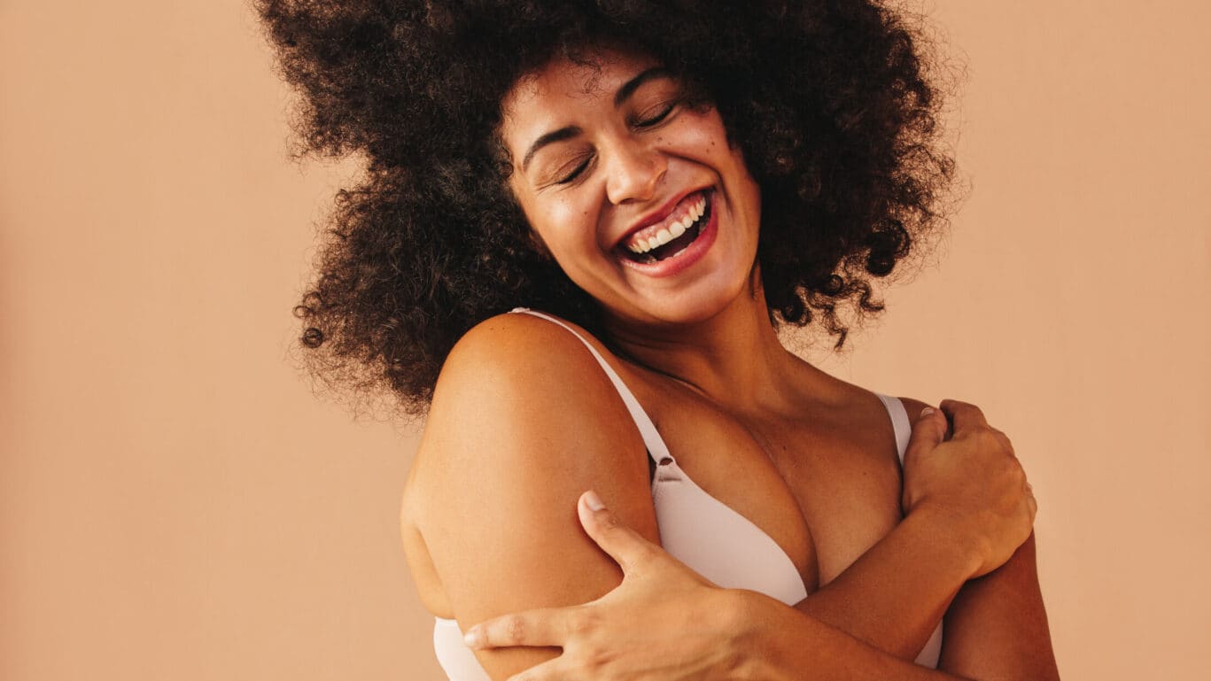 Happy woman clasping her hands to her chest wearing a light pink bra