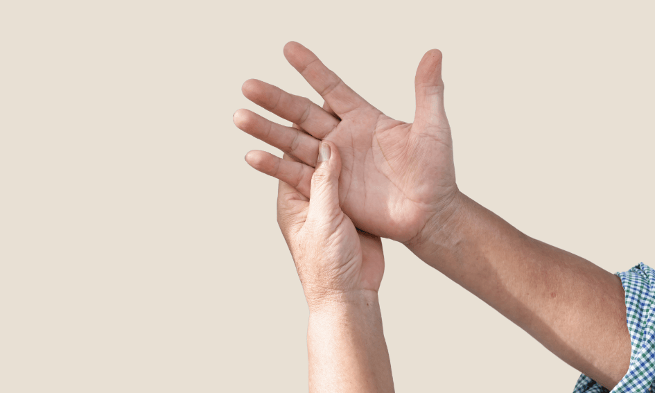 A specialist demonstrates proper hand massage techniques, using their right hand to gently massage the palm of their left hand, set against a light beige background.